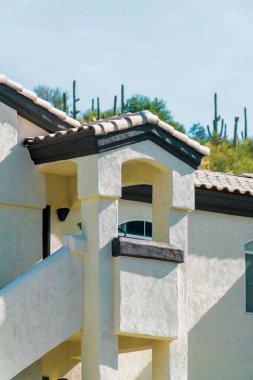 Modern apartment building with white stucco exterior with red tiles in suburban part of the neighborhood downtown. Visible hill with cactuses and light blue sky background in ubrna part of city.