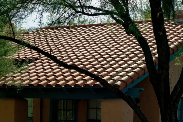 Large adobe style roof tiles with slanted double gable architecture in late evening shade and sun with front yard tree. In the neighborhood or downtown city on house or home in the town.