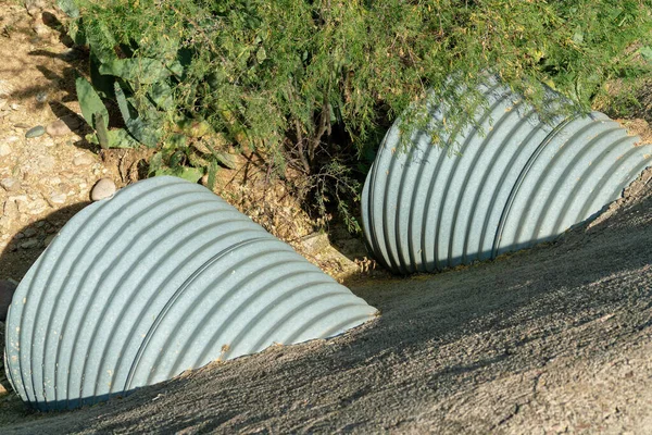 Metal rain gutter drainage pipes used to keep areas from flooding during a downpour or storm in an industrial area. In sun with trees and plants in an urban area for run off during wet seasons.