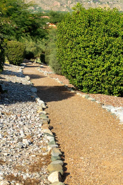 Hidden path or walkway in the neighborhood for walking dogs or for joggers and runners in a suburban community. Rock garden in sun with bushes and shrubs with sand in desert area.