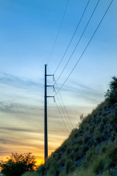 Early morning sunrise below the hills of nature and power line towers used for communication and energy transportation. In sunset with blue sky and rolling ridge hills in natural area of wilderness.