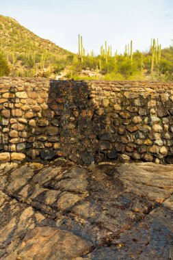 Retaining wall made of stone on waterfall or river for a stream of liquid running off from the mountains in sabino nationl park. In late afternoon sun with shade and saguaro cactus and mountains.