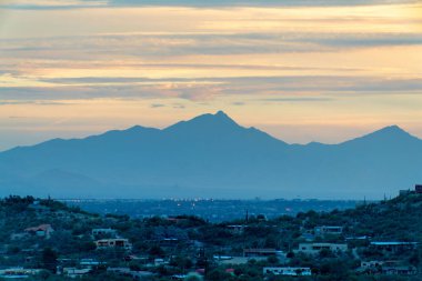 Sprawling mountain wilderness sunset with houses and homes in desert neighborhood with orange skies and blue clouds. In evening sun or sunrise in the cliffs and hills of tuscon arizona wilderness.