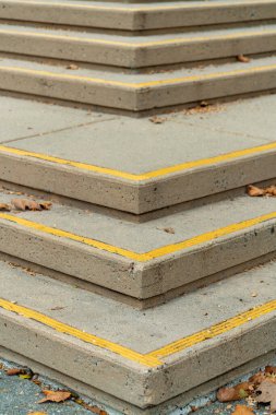 Row of stair edges with yellow paint on side of steps in modern city for pedestrians with visible autumn leaves in shade. Late in the season and midday shade in urban business districts.