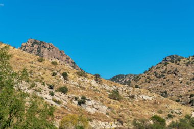 Mountainous cliffs in the wild western hills of outdoor arizona sonora desert in bright sunny afternoon light with blue sky. In the woods or wilderness with cactuses and vegetation.