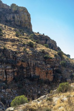 Tall rocky mountain surface with formations of stone for climbing and tourist atraction in late afternoon shade blue sky. Late in the day with shrubs and vegetation in wild west great outdoors area.