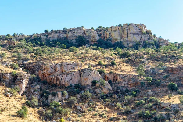 Sheer cliff faces in the hills and ridges of great outdoors in wild western arizona late in afternoon shade and sun. Hazy blue and white sky with visible cactuses and vegetation.