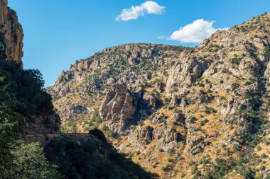 Rolling mountain hills with shadow ridges in the cliffs in late afternoon sun with clouds and blue sky. Late in the day in great outdoors in wilderness and roads in the hills.