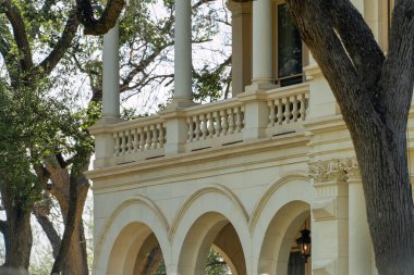 Decorative victorian or southern house and building facade in front yard with decorative flowering trees and white exterior. In afternoon shade with hazy gray sky and archways in neighborhood.