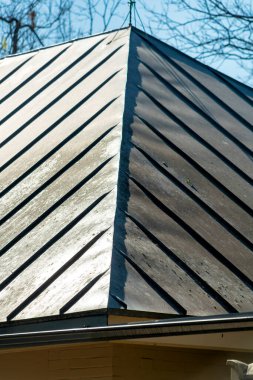 Tin roof with geometric lines on top of house or home in modern neighborhood or suburban part of midday city. Background trees in front or back yard with hazy white and blue sky urban downtown.