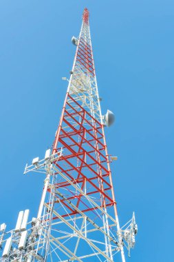 Radio or observance internet tower with white and red paint and satelite dishes on side of industrial exterior on blue sky. In urban area of city for 5g for future connectivity for neighborhood.