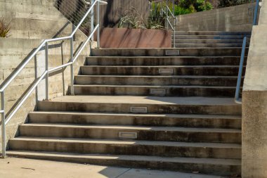 Row of industrial stares in city center in frotn of building or in apartment complex entrance in suburban areaa. Metal hand rail near steps in shade and sun and stone cement wall.