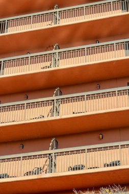 Row of tall balconies with metal hand rails on urban building for hotel or business with orange red facade or exterior. In late afternoon sunlight with shade in downtown heart of modern city.