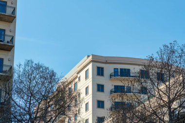 Downtown hotel or office building in san antonio texas in midday sun with some shade and winter dead trees in front yard. In the city with hazy white blue sky in urban industrial area for travelers.