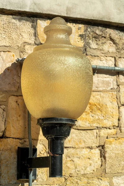 Industrial light or street lamp with beige or cream colored white stone bricks on side of building or structure. Late afternoon sun with black painted metal housing or post to light darkness.