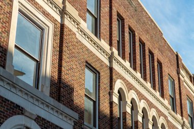 Early morning brick facade with visible windows and white accent paint on side of structure or building in downtown city. Late in the day evening sun with blue sky in urban suburban town.