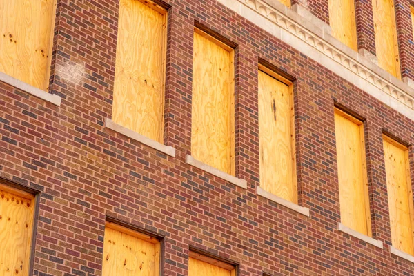 Boarded up building with wood on red or orange brick structure in late afternoon shade in downtown neighborhood. Abandonded and left to disrepair in suburban town for real estate disaster ohio.
