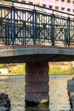 Cement walkway with decorative brick facade on bridge with metal hand rails and sunny background in canal and river waters in uraban setting. In downtown city neighborhoods or suburban area.