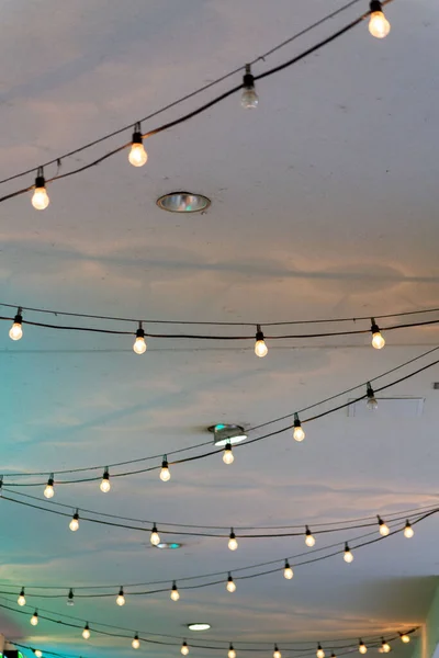 Row of string lights and white stucco building facade ceiling with zig zag fashion or designk inside a building or mall. Indoors with recessed lighting in city or urban area for commerce.