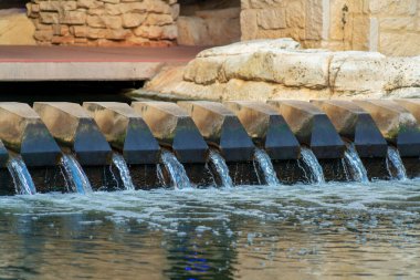 Water filter and dam used as decorative diversion in commercial districts for pool or canal in city neighborhood. Rock and stones facades on water rake for parting liquid in afternoon shade.