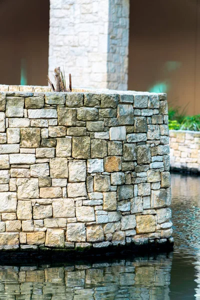 Stone wall with beige white decorative bricks and rocks in afternoon shade near pool or canal in industrial urban area of city. Near a mall or commercial outdoor districts in neighborhood downtown.