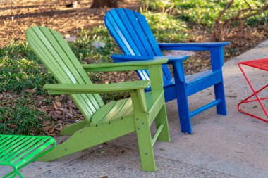 Colorful chairs on deck or patio in the back or front yard with green and blue seats on cement sidewalk in neighborhood home. House in city with urban or suburban barbeque lounge with green grass.