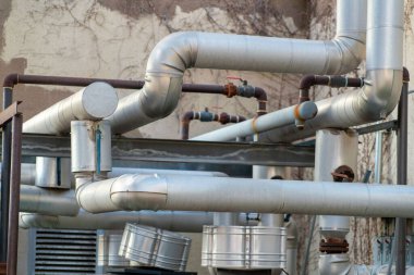 Row of industrial pipes in factory or manufacturing building in the hearth of downtown city neighborhoods with generators. Late afternoon shade for construction and development in town.