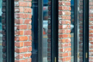Row of glass windows with red exterior brick facade in late afternoon shade in city or downtown area of neighborhood. Urban planning in city storefront or business districts for office or bulilding structures.