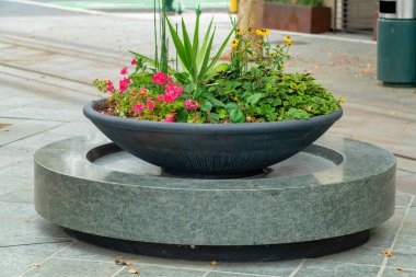 Planter on statue in urban area of city with pink and green flowers vegetation and foliage tropical in downtown part of suburbs. In city neighborhood for decoration and livening up sidewalks in urban areas.