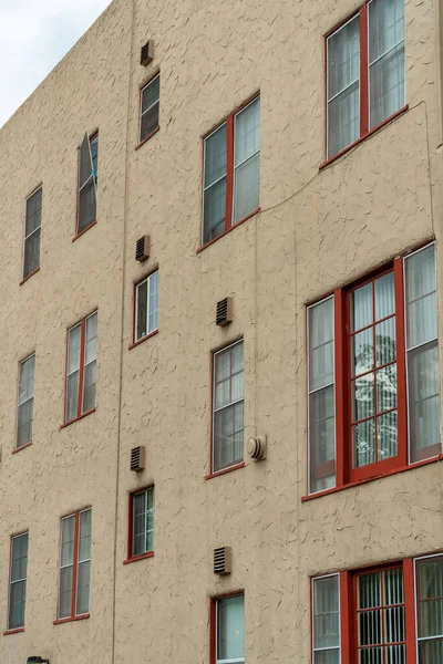Building exterior with orange or beige stucco cement facade and red accent paint around window frames with visible glass. Late afternoon shade in residential districts of modern american city.