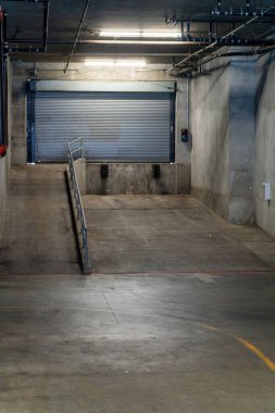Boş bir otopark ya da kamyonların şehir merkezindeki bir dükkâna ya da iş yerine mal taşımaları için depo. Kapısı, kapısı ve tırları olan beton zemin..