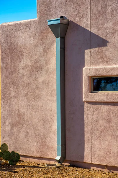 アドベ式セメントスタッコビルベージュと小さな窓と赤の外観の側に装飾的な金属雨のガター アリゾナの砂漠の近所で土と青空と午後遅くの日没の太陽 — ストック写真