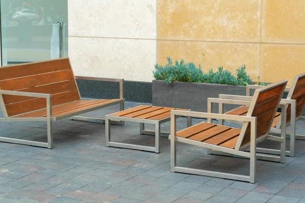 Rest area outside of office building with cement walls yellow and beige with brown wooden benches and table on sidewalk. Late afternoon shade in downtown urban or suburban areas of town.