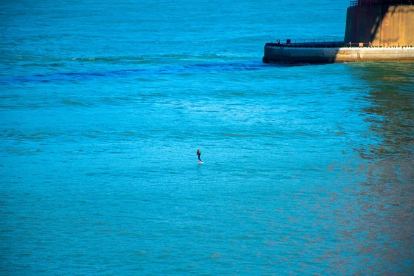 Man on hydrofoil on waterfront underneath the golden gate brich island platform with cement on waves in late afternoon sun. In tourist area for recreation in natural beach front in water.