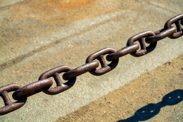 Large metal steel or iron chain made of titanium with individual links and rusted over with weather and age in downtown city. Background cement with visible shadows for background or texture purposes.