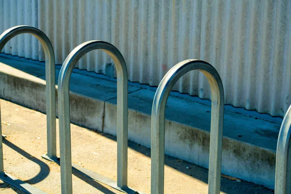 Metal bike rack arches for securing and chaining bicycle on side of metal building in urban downtown area of city. In afternoon shade for preventing theft and fighting climate change by riding.