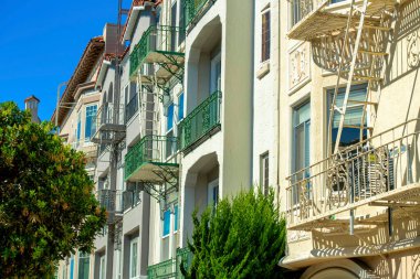 Şehir merkezindeki apartman binası dekoratif ön cephelerle ve pencereli ve balkonlu beyaz dış cephelerle kaplıdır. Evlerinin bahçesinde ağaçlar olan banliyö mahallelerinde.