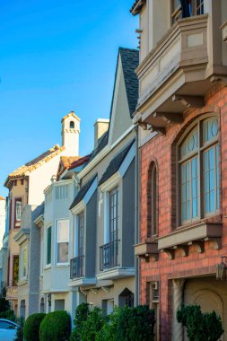 Duvarları tuğlalı, mavi beyaz bej renkli ve açık mavi gökyüzü ile öğleden sonra gölgeli modern evler. Şehir merkezindeki caddelerde camları ve beyaz aksanlı çerçeveleri olan bir mahalle..