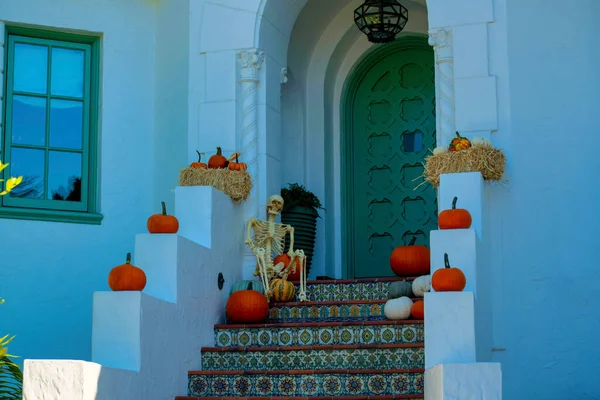 Front door entrance or stoop staircase with decorative autumn halloween squashes pumpkins with skeleton holiday. For october trick or treat in neighborhood with white stucco cement house in shade.