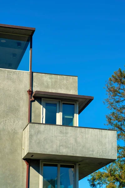 セメント近代的なスタイルの家や窓や前庭の木とフラット屋根とバルコニー付きのダウンタウンの都市の近所の家 午後遅くの太陽の光とコピースペース青空の背景 — ストック写真