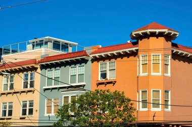 Şehir merkezindeki San Francisco tarihi bölgelerindeki renkli apartman binaları ya da kasaba evleri. Turuncu bej ve yeşil cepheli ön bahçe ağaçları uzay mavi gökyüzünü kopyalıyor.