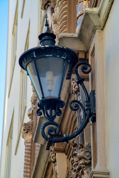 Black metal light post in midday shade with visible bulb in industrial commercial and residential part of town. Building facade exterior with outdoor lighting for dark areas of city at night.