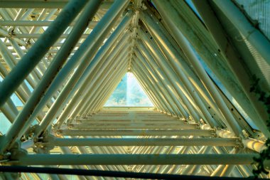 Geometrik tünel, üçgen metal kirişler ve sera binasında iskeleler ya da camdan yapılar. En sonunda koyu gölge çubuklarıyla dışarıda ışık olan alanın sonuna bak.