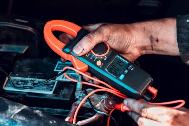 Kirli erkek araba tamircisi elleri elektrikçi multimetresiyle kaputun altında çalışıyor..