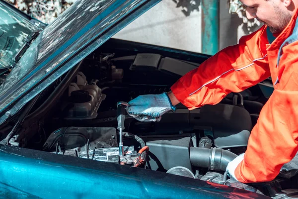 Vehicle maintenance. Male mechanic wears uniform and working under car hood in garage.