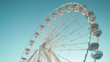 Dönme dolap. Lunaparkta aile eğlencesi. Beyaz dönme dolap temiz mavi gökyüzünde dönüyor. Dönme dolaba yakın çekim ve aydınlatma.. 