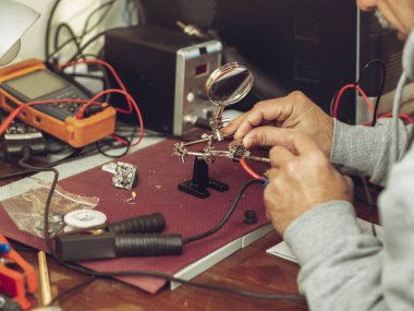 Home workshop and small business.Electronics engineer repaired with soldering using soldering station with hot gun iron and Third Hand Soldering clamps.