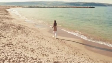 Soğuk sonbahar kumsalında koşan genç ve güzel bir kadının hava manzarası. Kız okyanusta koşuya çıktı.