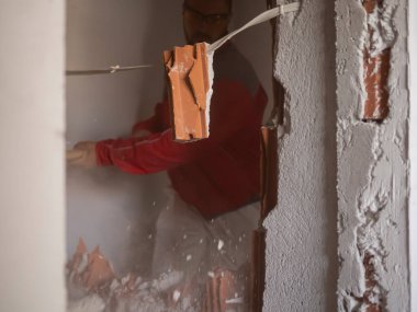 Yıkım işleri ve ev tadilatı. İnşaat işçisi bir balyozla duvarı parçalıyor. Alçı parçacıkları ve tuğla parçaları güçlü bir darbeden farklı yönlere dağılır.