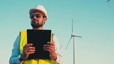 Wind turbines generate green energy with zero carbon footprint. Engineer holding a clipboard and inspecting the windmill park